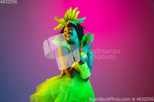 Image of Beautiful young woman in carnival and masquerade costume on gradient studio background in neon light