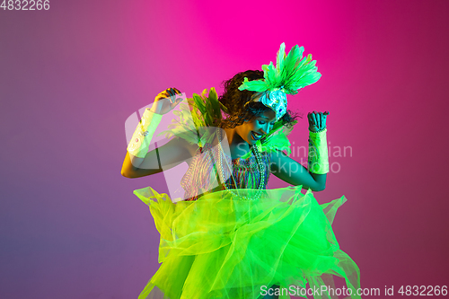 Image of Beautiful young woman in carnival and masquerade costume on gradient studio background in neon light