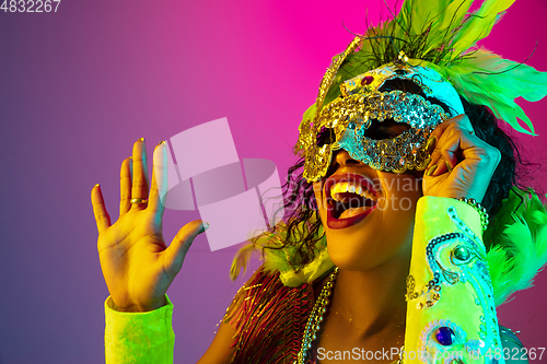 Image of Beautiful young woman in carnival and masquerade costume on gradient studio background in neon light