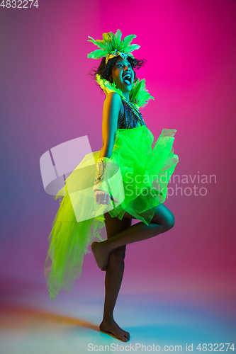 Image of Beautiful young woman in carnival and masquerade costume on gradient studio background in neon light