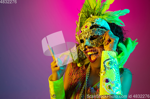 Image of Beautiful young woman in carnival and masquerade costume on gradient studio background in neon light