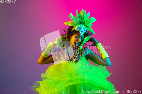 Image of Beautiful young woman in carnival and masquerade costume on gradient studio background in neon light