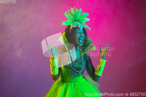 Image of Beautiful young woman in carnival and masquerade costume on gradient studio background in neon light