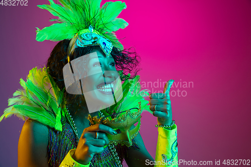 Image of Beautiful young woman in carnival and masquerade costume on gradient studio background in neon light