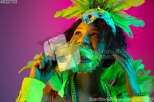 Image of Beautiful young woman in carnival and masquerade costume on gradient studio background in neon light