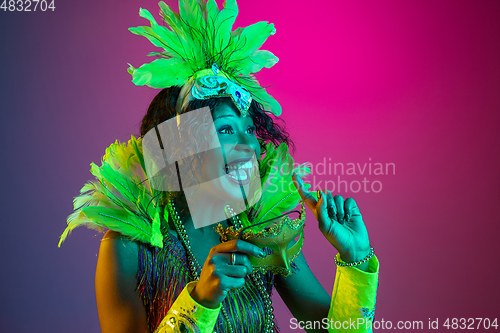 Image of Beautiful young woman in carnival and masquerade costume on gradient studio background in neon light