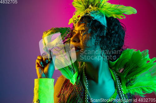 Image of Beautiful young woman in carnival and masquerade costume on gradient studio background in neon light