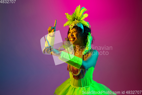 Image of Beautiful young woman in carnival and masquerade costume on gradient studio background in neon light