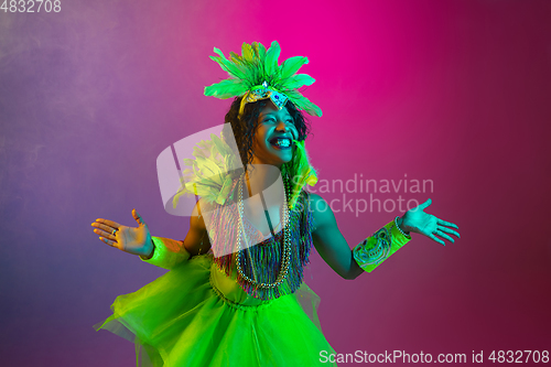 Image of Beautiful young woman in carnival and masquerade costume on gradient studio background in neon light