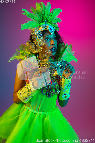 Image of Beautiful young woman in carnival and masquerade costume on gradient studio background in neon light