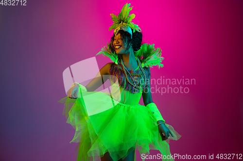 Image of Beautiful young woman in carnival and masquerade costume on gradient studio background in neon light