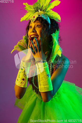 Image of Beautiful young woman in carnival and masquerade costume on gradient studio background in neon light