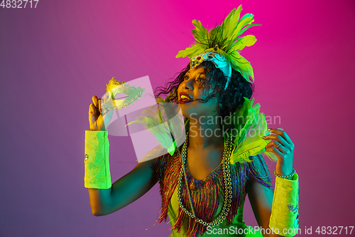 Image of Beautiful young woman in carnival and masquerade costume on gradient studio background in neon light