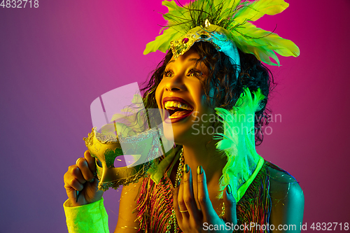 Image of Beautiful young woman in carnival and masquerade costume on gradient studio background in neon light