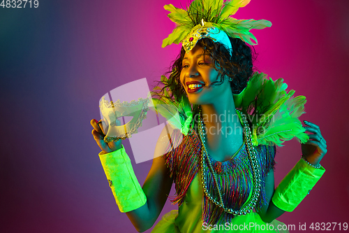 Image of Beautiful young woman in carnival and masquerade costume on gradient studio background in neon light