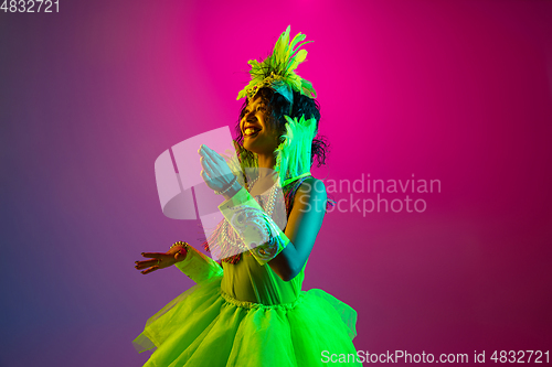 Image of Beautiful young woman in carnival and masquerade costume on gradient studio background in neon light