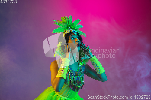 Image of Beautiful young woman in carnival and masquerade costume on gradient studio background in neon light