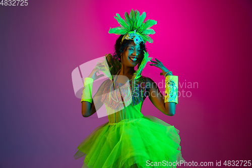 Image of Beautiful young woman in carnival and masquerade costume on gradient studio background in neon light