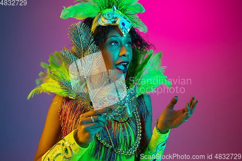 Image of Beautiful young woman in carnival and masquerade costume on gradient studio background in neon light