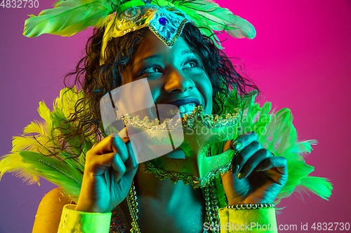 Image of Beautiful young woman in carnival and masquerade costume on gradient studio background in neon light