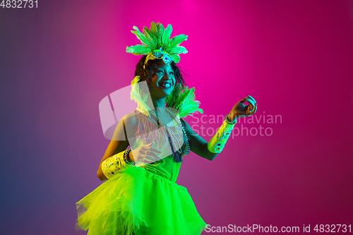 Image of Beautiful young woman in carnival and masquerade costume on gradient studio background in neon light