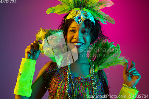 Image of Beautiful young woman in carnival and masquerade costume on gradient studio background in neon light