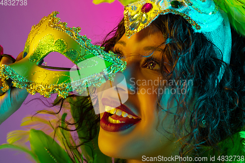 Image of Beautiful young woman in carnival and masquerade costume on gradient studio background in neon light