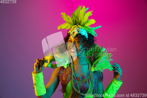 Image of Beautiful young woman in carnival and masquerade costume on gradient studio background in neon light