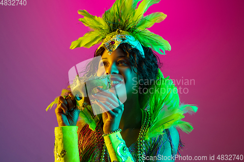 Image of Beautiful young woman in carnival and masquerade costume on gradient studio background in neon light