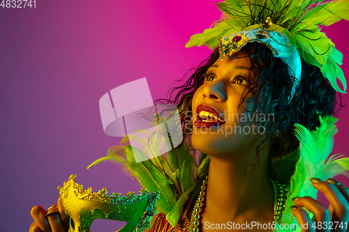 Image of Beautiful young woman in carnival and masquerade costume on gradient studio background in neon light