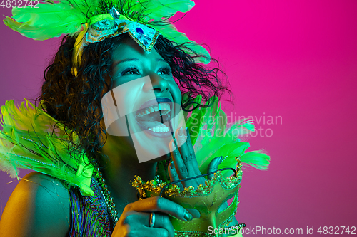 Image of Beautiful young woman in carnival and masquerade costume on gradient studio background in neon light