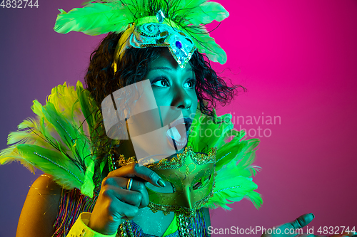 Image of Beautiful young woman in carnival and masquerade costume on gradient studio background in neon light