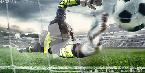 Image of African male soccer or football player, goalkeeper in action at stadium. Young man catching ball, training, protecting goals in motion.