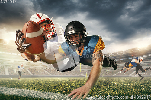 Image of American football players in fight for goal at stadium in flashlights. Professional sportsman during game playing in action and motion.