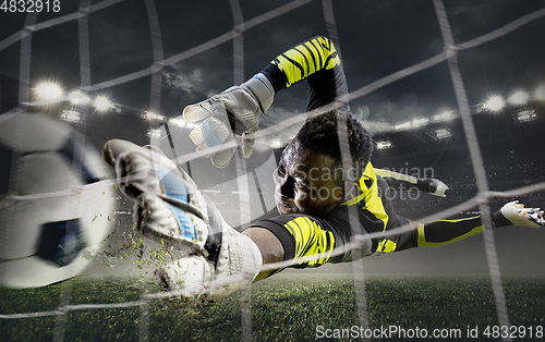 Image of African male soccer or football player, goalkeeper in action at stadium. Young man catching ball, training, protecting goals in motion.