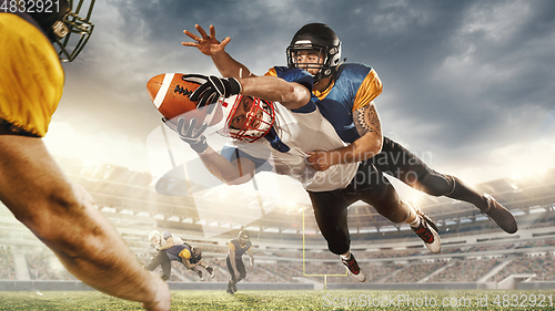 Image of American football players in fight for goal at stadium in flashlights. Professional sportsman during game playing in action and motion.