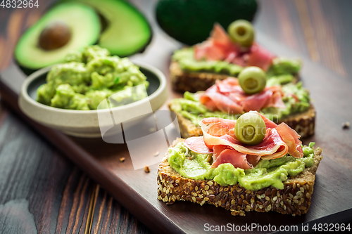 Image of Guacamole dip or spread with open sandwiches and ham on wooden kitchen table