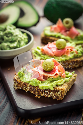 Image of Guacamole dip or spread with open sandwiches and ham on wooden kitchen table