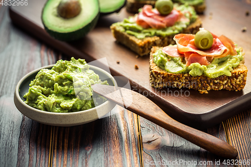 Image of Guacamole dip or spread with open sandwiches and ham on wooden kitchen table