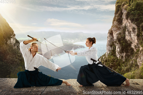 Image of Man and woman, teacher fighting Aikido, training martial arts on meadow in front of lake and mountains