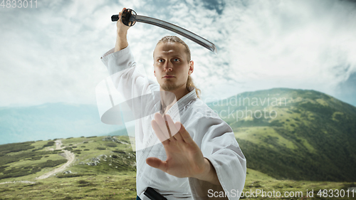 Image of Young man, teacher fighting Aikido, training martial arts on meadow in front mountains