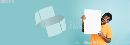 Image of Young African man with blank sheet of paper isolated over blue studio background.