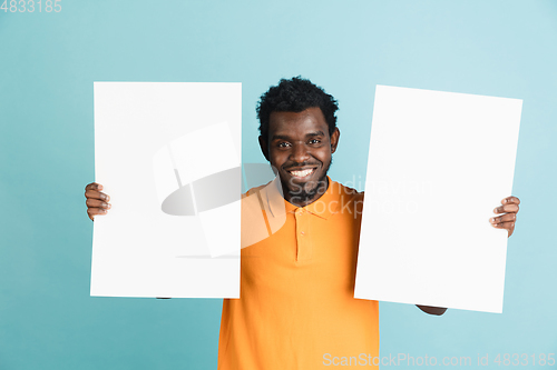 Image of Young African man with blank sheets of paper isolated over blue studio background.