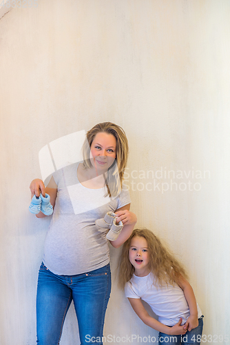 Image of Pregnant woman holding blue baby booties with her daughter