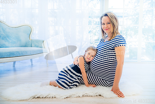 Image of Beautiful pregnant woman with daughter sitting near the window