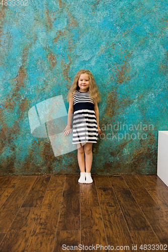 Image of Cute girl in striped clothes standing near the wall