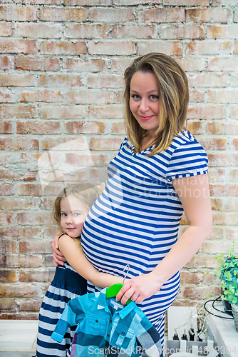 Image of Beautiful pregnant woman with daughter near the wall