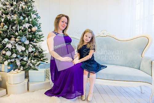 Image of Beautiful pregnant woman in an ultraviolet dress sitting with daughter