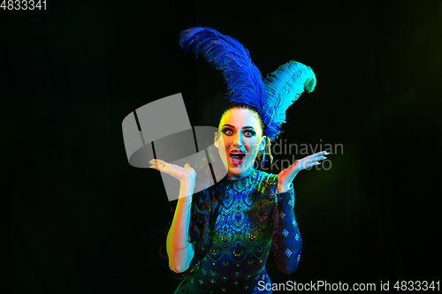 Image of Beautiful young woman in carnival and masquerade costume in colorful neon lights on black background