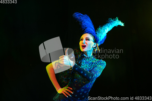 Image of Beautiful young woman in carnival and masquerade costume in colorful neon lights on black background